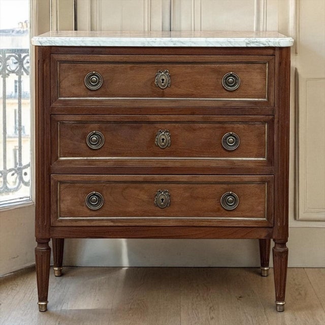 French Louis XVI Mahogany Marble Top Commode is an elegant design including a white marble top, three drawers, and...