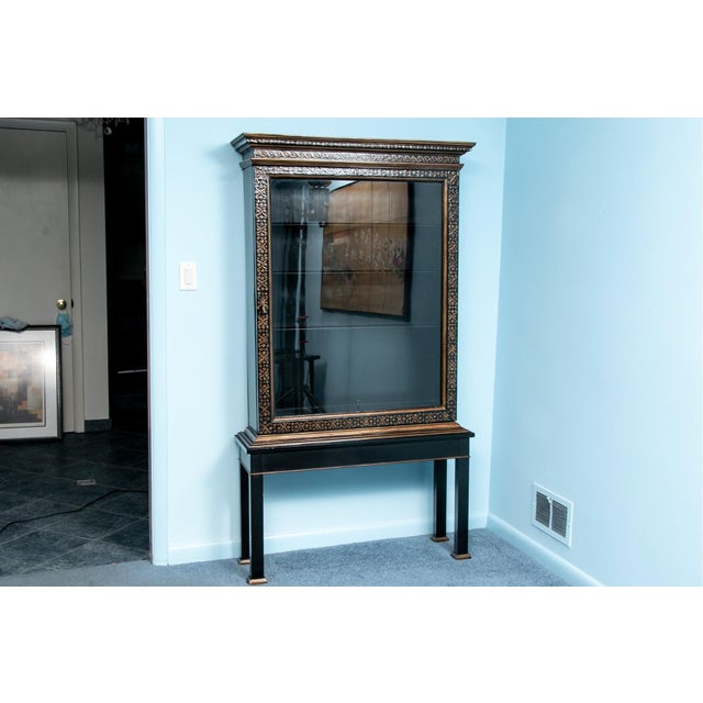 A vintage French Louis XVI glass front vitrine display cabinet made of ebonized mahogany and elaborately trimmed in gilt...