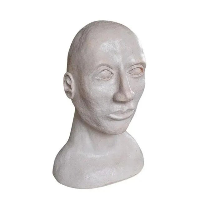 A large hand-sculpted bust of a man. Created from white clay, this piece is life-size and depicts a man who stares off...