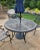 Like new - Outdoor dining set in wrought iron includes a round table and 4 arm chairs in a deep gray finish. Chair...