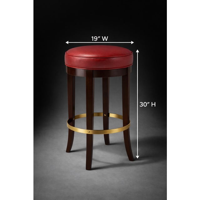 A classic club-style bar stool featuring an oversized red leather swivel seat, richly finished mahogany legs, and a...