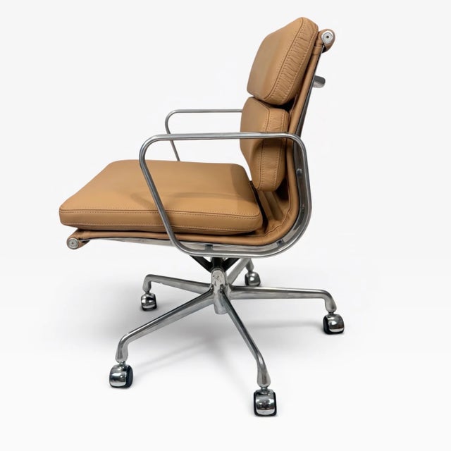 A classic Eames Soft Pad Management Chair upholstered in warm camel brown leather with a polished aluminum frame. The...