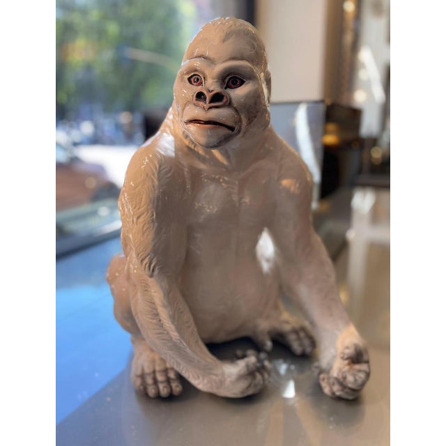 Decorative statue of a seated gorilla, made of ceramic with a glossy white finish. The gorilla has realistic details in...