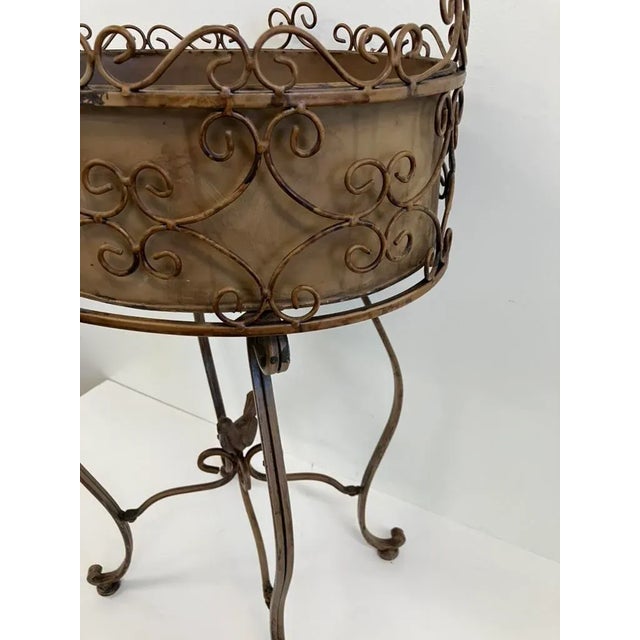 This vintage wrought iron plant stand, dating from the mid-20th century (circa 1950s–1960s), features an ornate scrollwork...