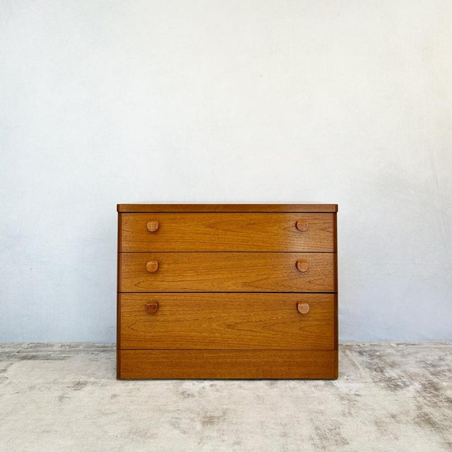 Teak-veneered carcase construction on a plinth base with rounded front corners. Three full-width graduated drawers....