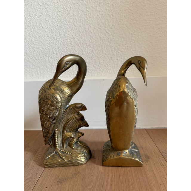A pair of brass swans, each rising out of a bed of foliate scrollwork, made to hold a shelf of books upright and to look...