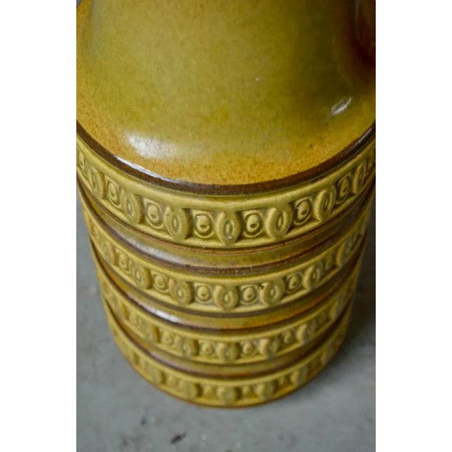 With its mustard yellow enamel decorated with repetitive geometric shapes in relief, its pitcher shape and its generous...
