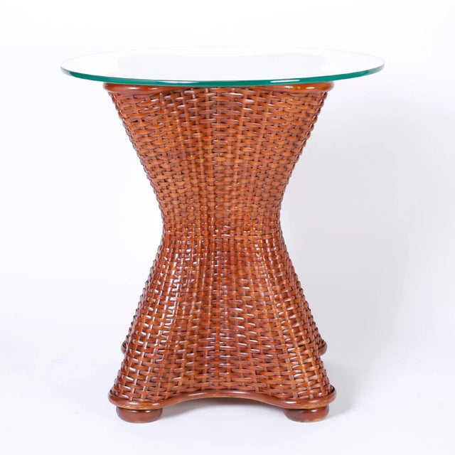 Midcentury wicker and rattan stands with round glass tops and a classic hour glass form on bun feet. Can also be used as a...