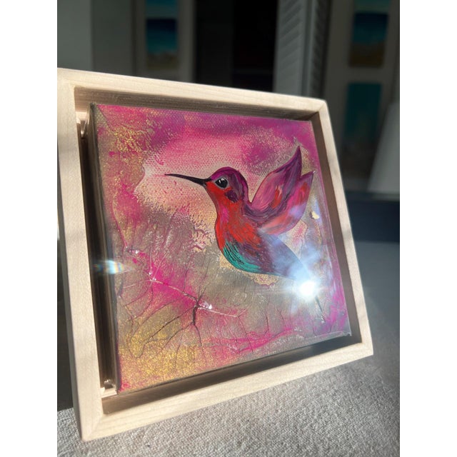 This artwork captures a vibrant hummingbird in mid-flight, rendered in rich hues of orange, pink, and teal. The layered...