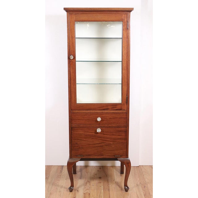 Vintage mahogany medical display cabinet in dark wood tones with glass shelves. Built tall and narrow to fit into tight...