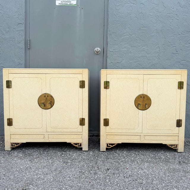 Elegant pair of vintage Chinoiserie server cabinets featuring warm cream finishes accented with fine gold detailing and...
