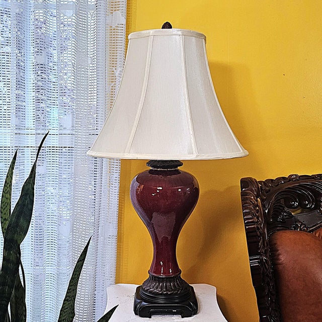 This vintage Bombay Company table lamp features a rich oxblood glazed ceramic urn base with a deep, lustrous finish and a...