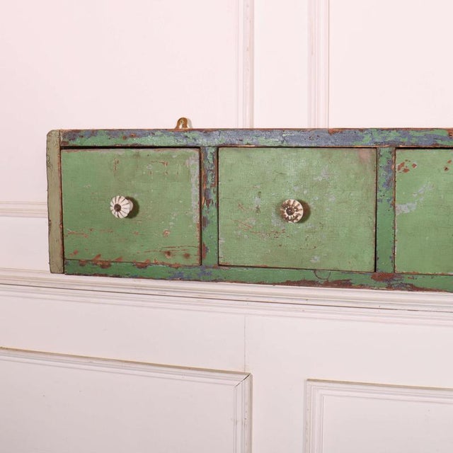 Interesting 19th C English wall hanging pine bank of drawers with old worn paint. 1890 This piece is designed in the style...