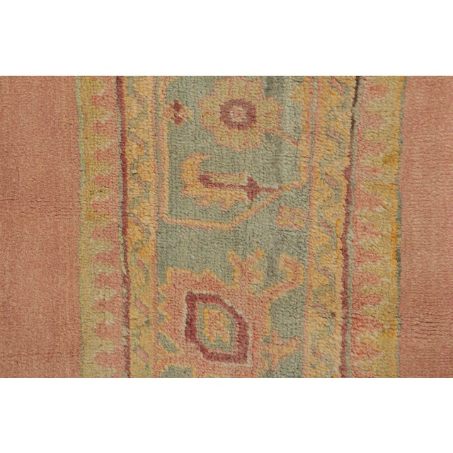 Handwoven in wool, circa 1920–1940, this antique 2x10 Oushak runner rug features a narrow floral corridor design in faded...
