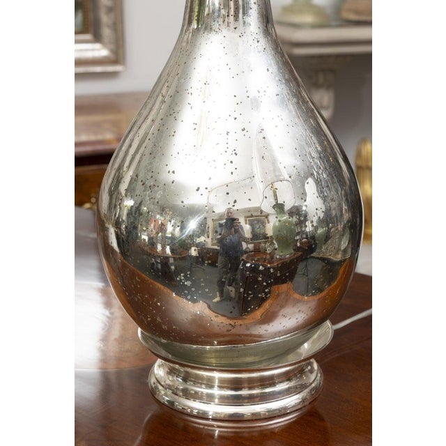 This is an elegant pair of tall mercury glass table lamps featuring elongated bottle-form silhouettes with slender ribbed...