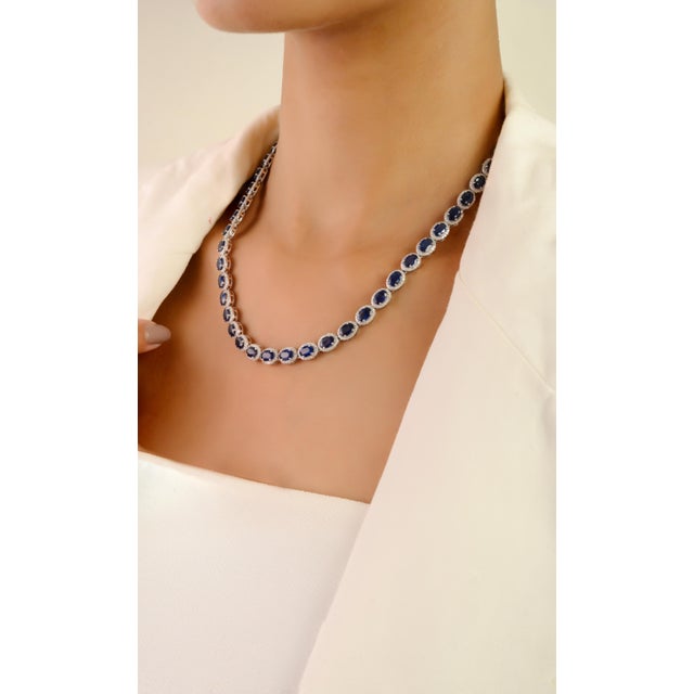 This luxurious tennis necklace showcases 27.67 carats of oval-cut blue sapphires, each encircled by a halo of 4.51 carats...