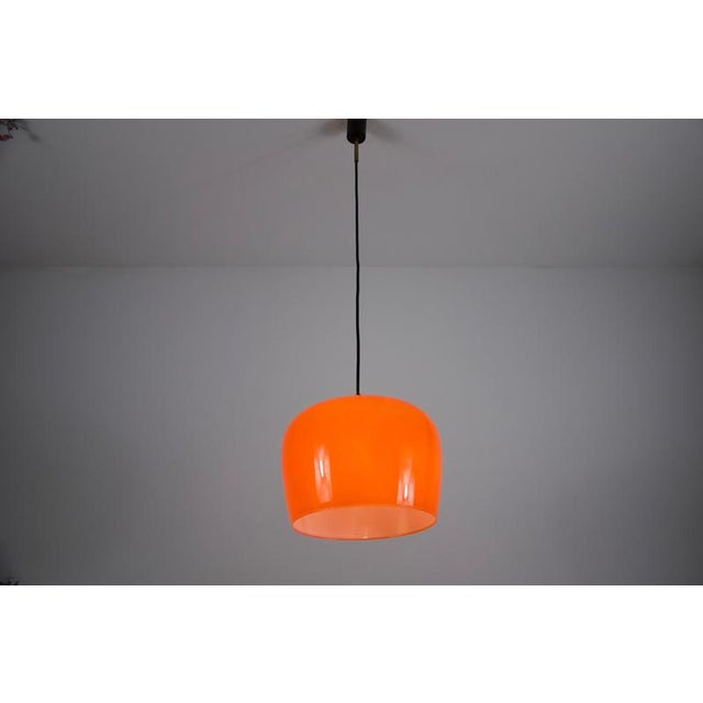 This modern pendant lamp features a smooth, rounded shade in a striking, translucent orange finish that brings warmth and...