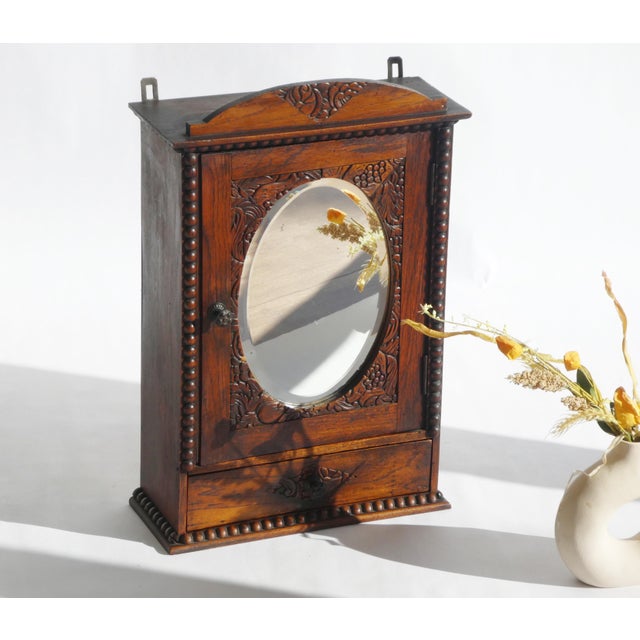 An antique Art Deco style wooden wall cabinet with an oval beveled mirror and nice floral carvings all around. The...