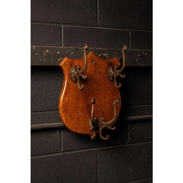 Victorian wall-mounted coat and hat rack featuring a warm-finished oak backboard cut in a heraldic shield form with a...