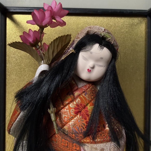 A striking vintage ichimatsu-style doll presented in a glass display case with a black lacquered wooden frame and an...