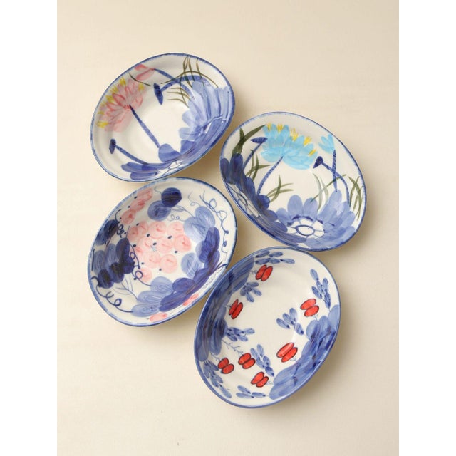 A set of four hand-painted blue-and-white ceramic bowls, each featuring a unique floral or botanical motif; the fresh blue...