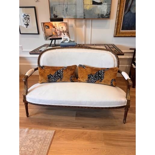 Louis XVI style canapé featuring a graceful oval back, open scrolled arms, and a finely carved painted and giltwood frame....