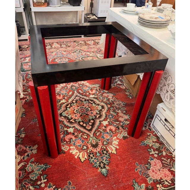 A striking architectural dining table with a clear glass top and a bold geometric base in red and black. The open...