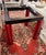 A striking architectural dining table with a clear glass top and a bold geometric base in red and black. The open...