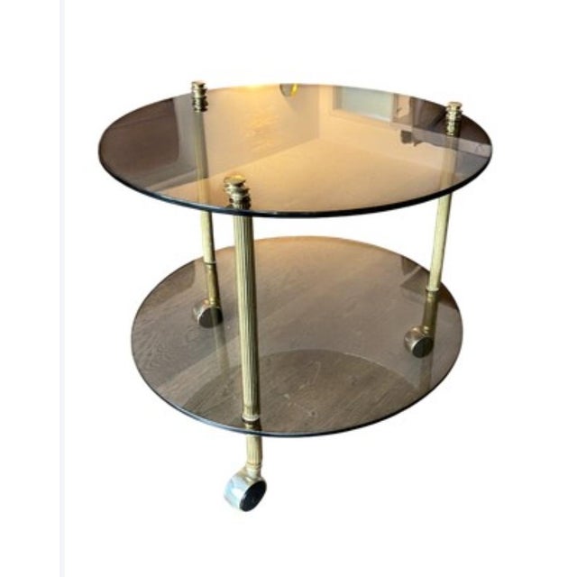 Elegant round coffee table in brass and tinted glass, composed of two glass tops supported by a cylindrical brass frame....