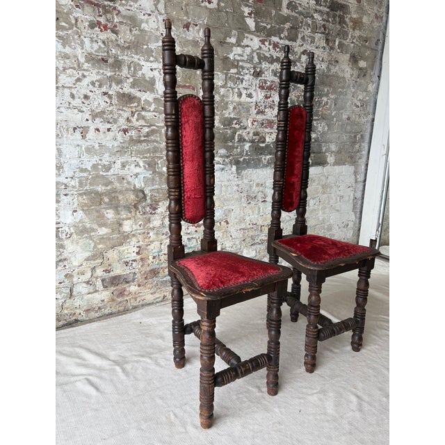 A striking pair of vintage prayer chairs featuring richly turned wood detailing, deep oxblood velvet upholstery, and hand-...