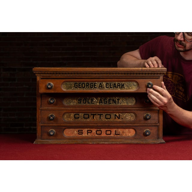 Four-drawer oak spool cabinet with reverse-painted glass advertising inserts reading "GEORGE A. CLARK / SOLE AGENT /...