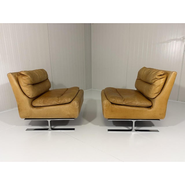 Set of 2 lounge chairs. Chrome plated metal frame, furnished in cognac leather, loose seat pilows, the back pillows are...