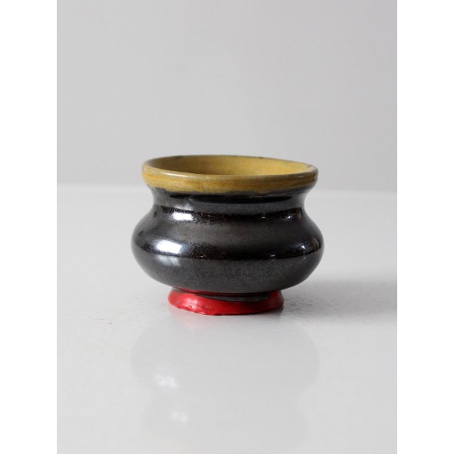 A vintage handmade studio pottery vase featuring a deep black glaze with a contrasting warm ochre interior. The rounded,...