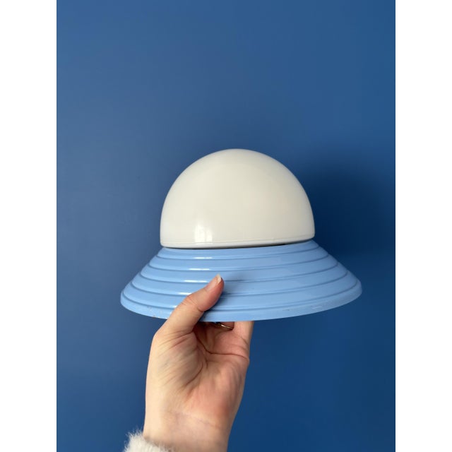 Stunning vintage wall sconce with a soft, graphic design, featuring a ribbed blue metal base and a white opaline glass...