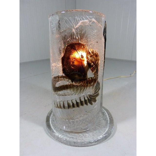 Table lamp by Mazzega, Italy. Thick colourless glass with in it brown/amber figures. On the glass foot are 2 half round...