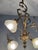 A beautifully ornate vintage chandelier featuring a golden frame with curving details and four frosted glass shades. Its...