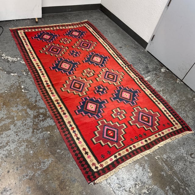 Design Plus Gallery presents a 5ft 8in × 10ft Turkish Kilim Area Rug. This flatweave wool rug displays a vivid red field...