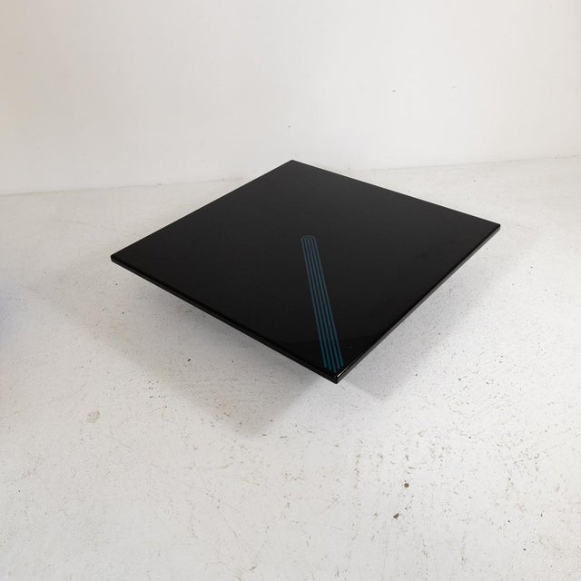 Large coffee table with a glossy lacquered wood top featuring a blue geometric pattern. The top rests on two lacquered...