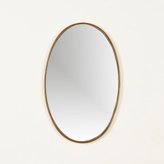 Elegant and refined oval wall mirror in solid brass, realized in Italy during the 1950s and inspired by the iconic designs...