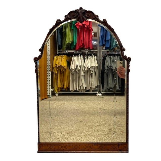 Vintage wall mirror featuring a tall arched form with an ornately carved wood frame. The crest showcases scroll and...