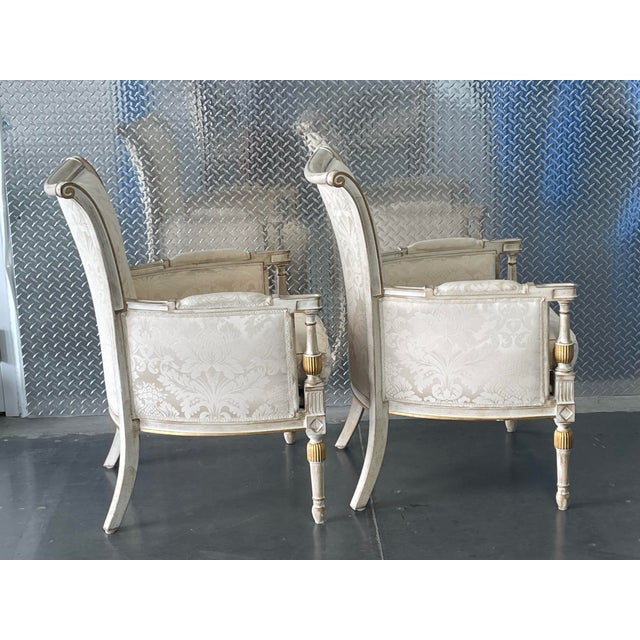 The chairs feature tall, gently flared shield backs with subtle scroll details at the crest, paired with square,...