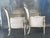 The chairs feature tall, gently flared shield backs with subtle scroll details at the crest, paired with square,...