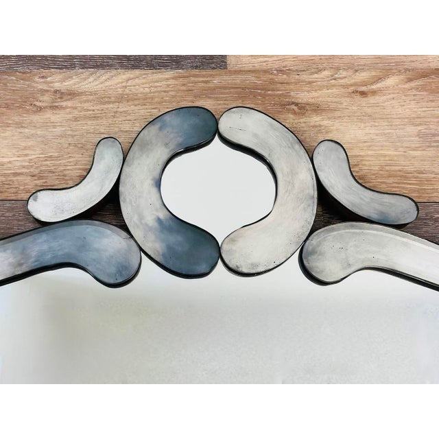 A large mid-century Venetian-style wall mirror with a dramatic, undulating silhouette and segmented smoky mirrored-glass...