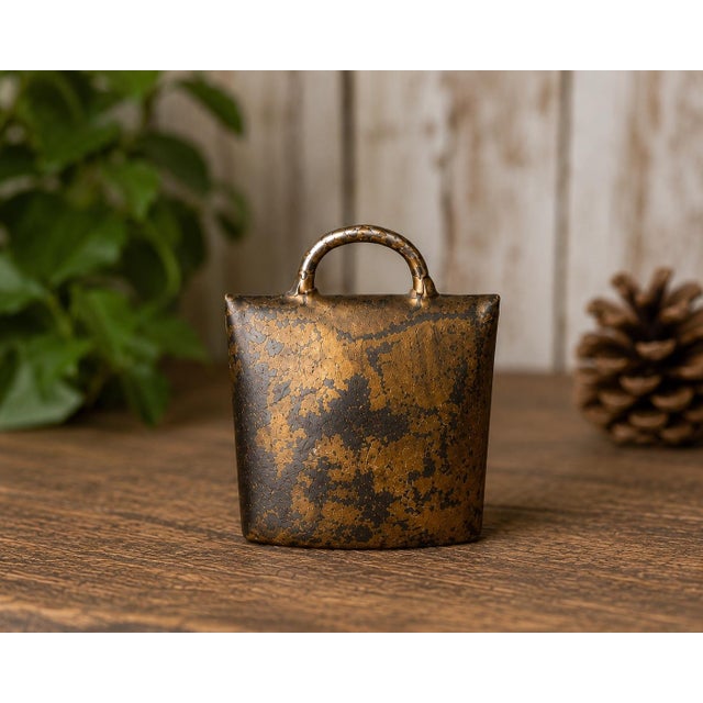 A wonderfully aged vintage German metal cowbell featuring a rich distressed gold-tone surface with deep blackened patina...