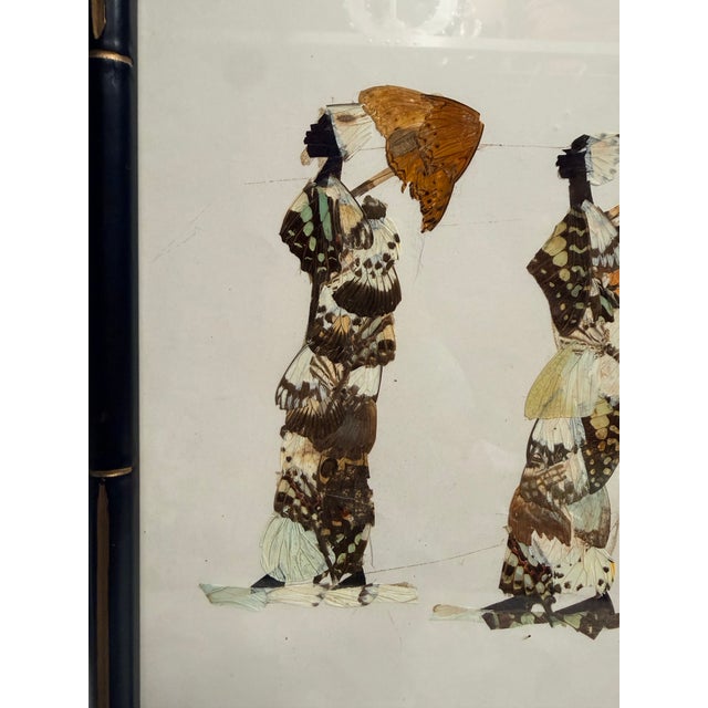 This unique framed artwork showcases two figures crafted entirely from butterfly wings, each holding a parasol. The...