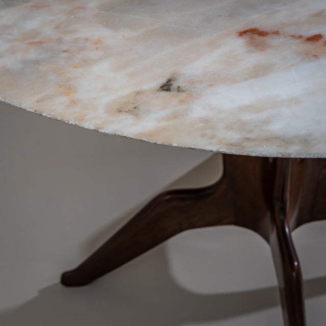 Round sculptural dining/center table made of wood and beige marble, featuring four splayed legs and a concave central column.