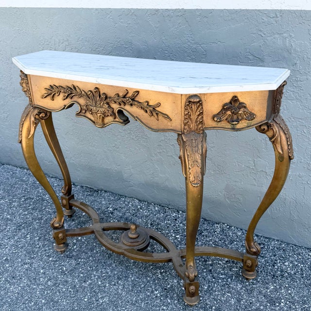 A striking vintage French style console table featuring an ornately carved giltwood base topped with a shaped white marble...