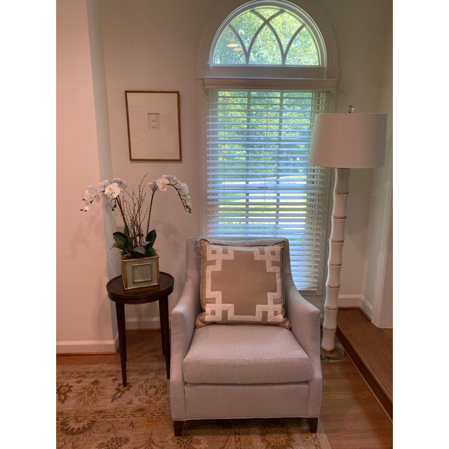 A tan cotton linen pillow, by Ryan Studio, in the chippendale style. The front features white grosgrain ribbon detailing....