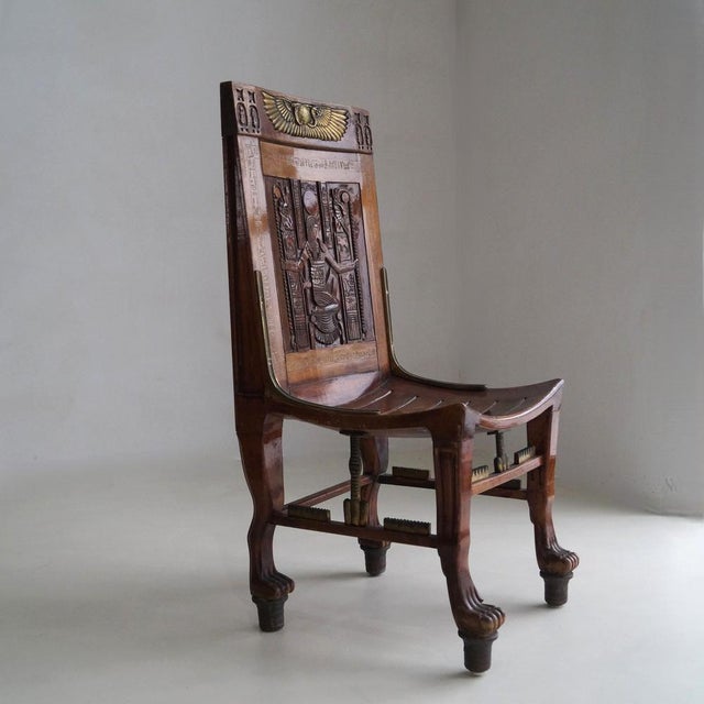 An impressive solid wooden Egyptian Revival chair with gilt accents and lion paw feet. Under the lion paw feet copper...