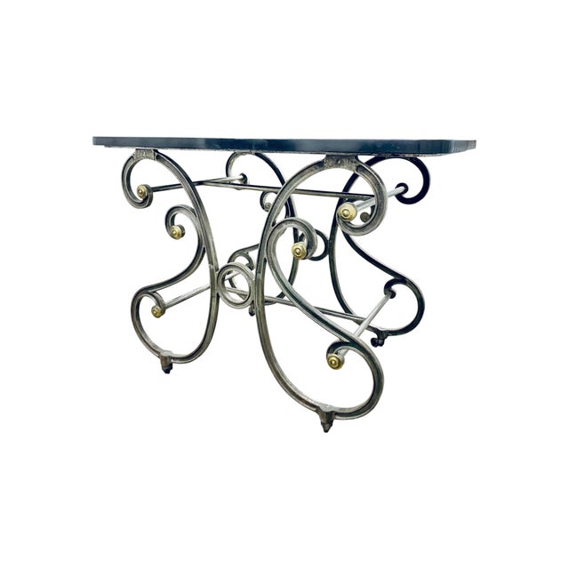 An antique French patisserie table featuring a distinctive black marble top and an ornate wrought iron base accented with...